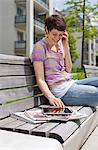 Young woman with cell phone and iPad on a bench