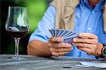 Senior man playing cards and drinking red wine, close-up