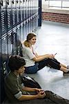 High school student sitting on floor by locker using cell phone