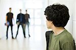 Teenage boy looking over shoulder at bullies in background