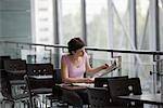 Young woman sits reading newspaper in food hall of shopping mall, Voronezh