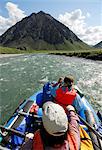 Two rafters rowing through a fast stretch of the Kongakut River on a sunny day with scenic mountains in the background, ANWR, Arctic Alaska, Summer