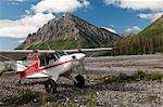 An Aviat Aircraft Husky A-1B rests on a gravel bar along the North Fork of the Koyukuk River with Frigid Crags looming in the background, Gates of the Arctic National Park & Preserve, Arctic Alaska, Summer