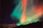 Multi colored Northern Lghts (Aurora borealis) fill the night sky and cast colored shadows on the mountain tops of Chugach State Park, Southcentral Alaska, Winter