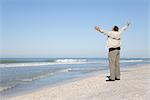 Homme debout sur la plage en regardant l'océan avec les bras tendus