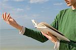 Young male reading aloud from book at the beach