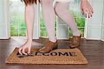 Woman picking up key on welcome mat in small room