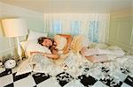 Young woman sleeping amongst pillow feathers in small room