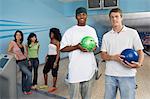 Group of friends at bowling alley, some holding balls, portrait