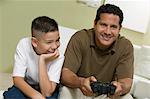 Son with father Playing Video Game on sofa in living room