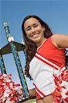 Smiling Cheerleader holding trophy, (portrait), (low angle view)