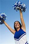 Smiling Cheerleader rising pom-poms, (low angle view)