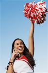 Smiling Cheerleader rising pom-pom, talking on mobile phone, (low angle view)
