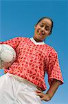 Girl (13-17) in soccer kit holding ball, portrait, low angle view