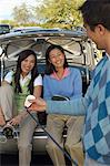 Mother and Daughter Sitting on Car Bumper Getting Ready to Golf, watching boyfriend show off golf club