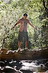 Teenage boy (16-17 years) walking tree trunk above stream