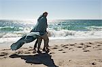 Mature couple walking on beach wrapped in blanket