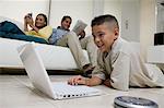 Boy Using Laptop on Floor in living room, mother and father on sofa, ground view