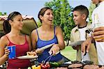 Boy (13-15) with family, gathered around grill at picnic.