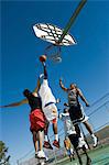 Two basketball players guarding another as he tries to shoot basketball, low angle view