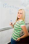 Female student writing equations on whiteboard, (portrait)