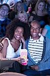 Young Couple sitting in theatre, arms around, Watching Movie, eating popcorn