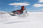 Couple jumping snowmobile in snow, mid air