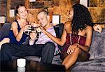 Man with two women toasting, sitting on couch in bar