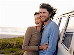 Young couple embracing by van parked by ocean, half length