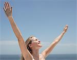 Young woman with arms outstretched and eyes closed on beach