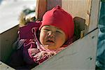 Greenland,Ittoqqortoormiit. A baby sitting in a pram in the isolated village of Ittoqqortoormiit (Scoresbysund) situated on the north east coast of Greenland. It receives 2 food deliveries per year.
