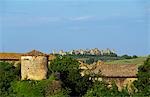 Toskanische Counrtyside mit Reben, Mandelbäumen und Wirtschaftsgebäude mit Mauern umgebene Stadt thront auf Hügel in der Nähe von Siena