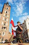 Man dressed as soldier holding Polish flag in parade to commemorate Warsaw Uprising on 1st August 1944 with St Mary's Church in background, Krakow, Poland