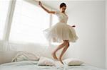 Young girl, teenager, having fun, jumping on bed in her white ballarina dress, in front of window, Salzburg, Austria, MR yes, PR no,