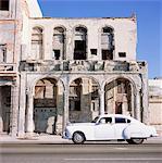 Classic white car passing rundown building