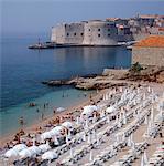Beach with rows of sun loungers with historic city wall in background
