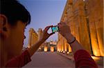 Woman taking photographs at dusk of papyrus-bundle columns in courtyard of Amenophis III