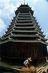 China, Guangxi Province, nr Sanjiang, Pinpu. A Dong woman moves baskets of ducks beside a traditional 'drum tower.'