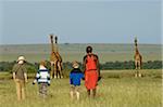Kenya, Masai Mara.  Safari guide, Salaash Ole Morompi, leads boys on a game walk towards some Masai giraffe.