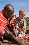 Kenya, Masai Mara.  Safari guide, Salaash Ole Morompi, shows a boy on safari how to light a fire with a stick and board.