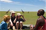 Kenya, Masai Mara.  Safari guide, Salaash Ole talks to boys on safari during a game drive out on the plains.