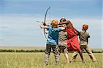 Kenia, Masai Mara. Safari-Führer, Salaash Ole Morompi, lehrt Kinder Bogenschießen Maasai-Stil.