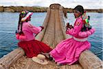 Peru, two girls from Uros row a reed boat to one of the unique floating islands of Lake Titicaca.