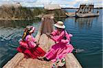 Peru, Two girl from Uros row a reed boat to one of the unique floating islands of Lake Titicaca.