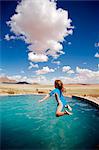 Sossusvlei Mountain Lodge, Namib Rand Nature Reserve, Namibia. A girl jumps into the pool with views towards the Desert.