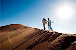 Sossusvlei, Namib-Naukluft National Park, Namibia. A young girl and a safari guide scale a sand dune in the Namib Desert.