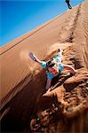 Sossusvlei, Namib-Naukluft National Park, Namibia. A young girl slides and tumbles down a sand dune in the Namib Desert.