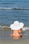 Baby-Mädchen sitzen am Strand tragen großer Sonnenhut