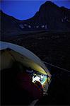 Woman in a tent at dusk consults a GPS and map while camping at Rabbit Lake, Chugach State Park, Southcentral Alaska, Autumn