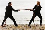 Two men dressed in suits in a tug-of-war on a beach.